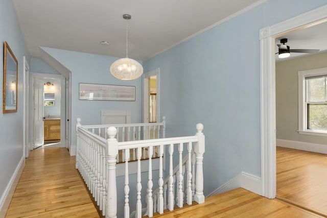 hallway featuring an inviting chandelier, light wood finished floors, baseboards, and an upstairs landing