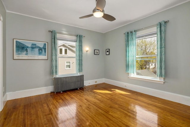 unfurnished room with ceiling fan, radiator, hardwood / wood-style floors, baseboards, and ornamental molding