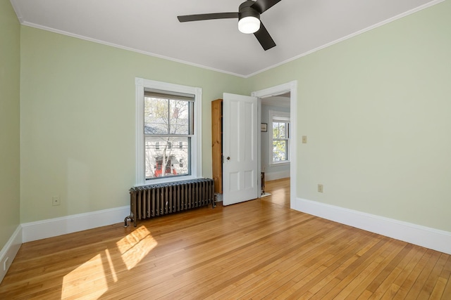 empty room featuring ceiling fan, ornamental molding, light wood-style flooring, and radiator