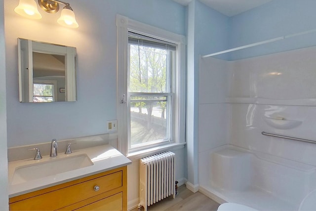bathroom with walk in shower, vanity, radiator, baseboards, and wood finished floors