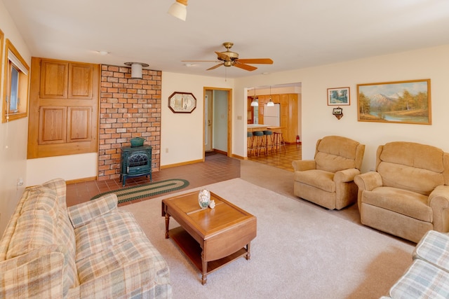 carpeted living area featuring baseboards, a wood stove, and ceiling fan