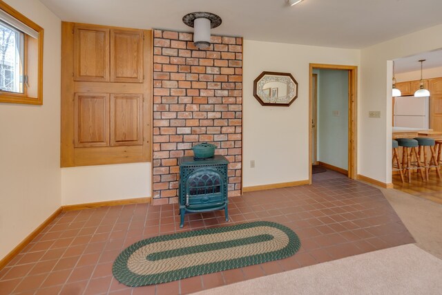 unfurnished living room featuring a wood stove, baseboards, and tile patterned flooring
