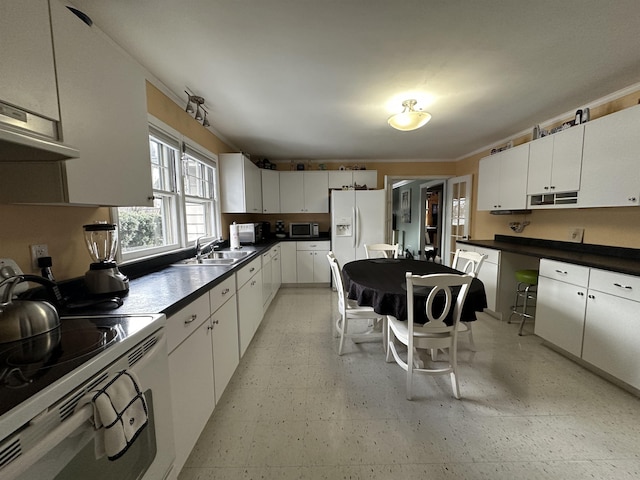kitchen featuring white cabinets, dark countertops, a sink, white appliances, and light floors