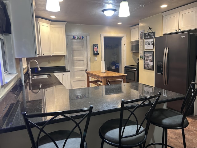 kitchen featuring a breakfast bar area, a sink, white cabinets, stainless steel appliances, and recessed lighting