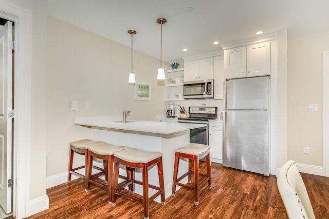 kitchen with a peninsula, a kitchen bar, a sink, dark wood finished floors, and appliances with stainless steel finishes