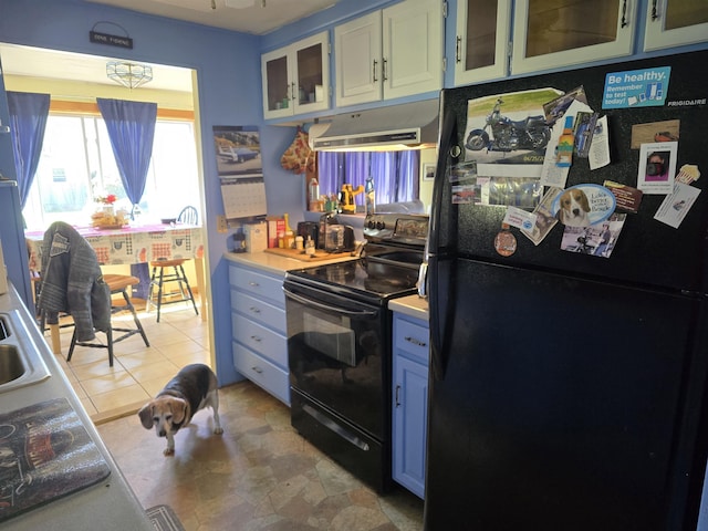kitchen featuring blue cabinetry, light countertops, black appliances, glass insert cabinets, and under cabinet range hood
