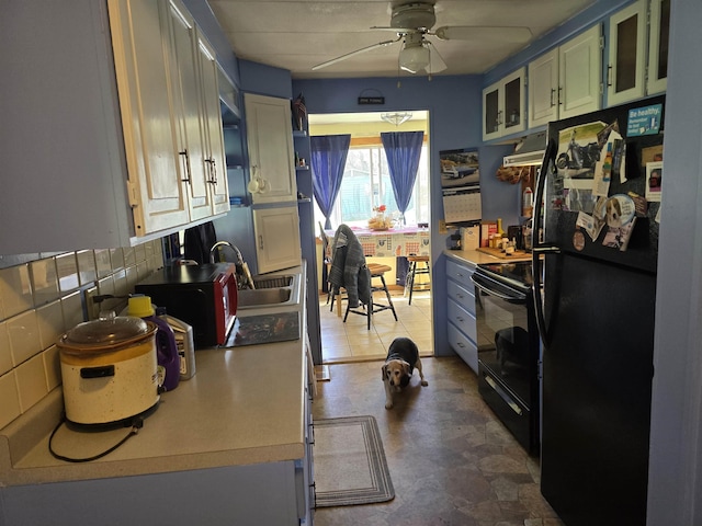 kitchen featuring a sink, a ceiling fan, under cabinet range hood, glass insert cabinets, and black appliances