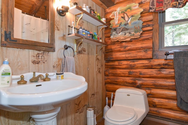 full bathroom featuring a sink, rustic walls, toilet, and curtained shower