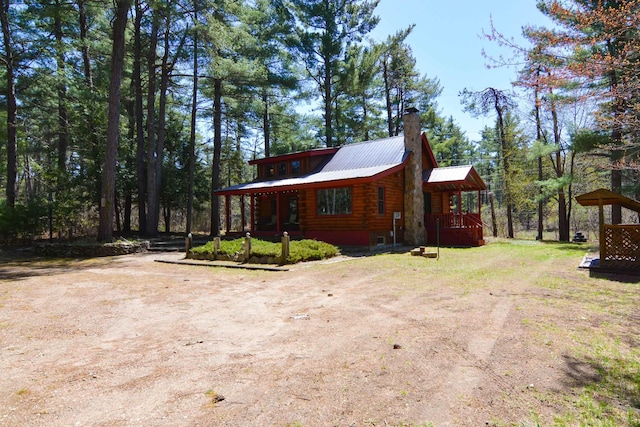 view of side of property featuring log siding, a chimney, metal roof, and dirt driveway