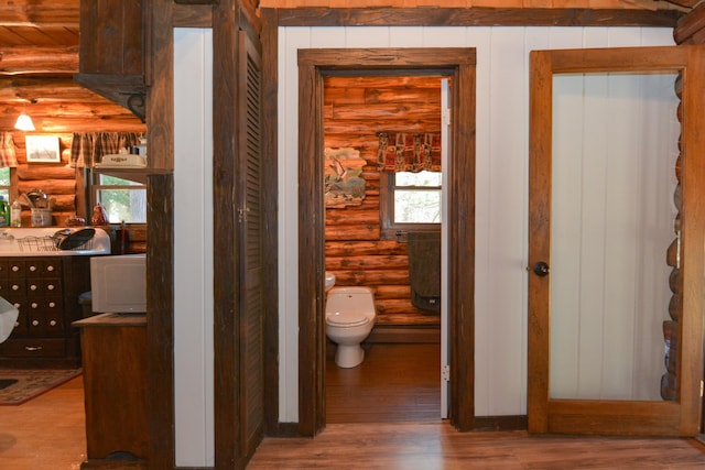bathroom with toilet, log walls, and wood finished floors