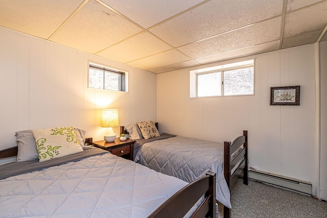 carpeted bedroom featuring a paneled ceiling, a decorative wall, baseboard heating, and multiple windows