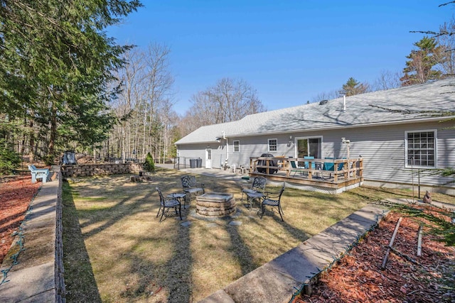 back of house featuring a yard, a deck, roof with shingles, and an outdoor fire pit
