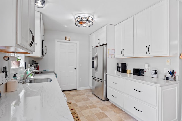 kitchen with light stone countertops, baseboards, stainless steel refrigerator with ice dispenser, white cabinetry, and a sink
