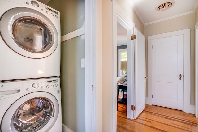 laundry room with laundry area, stacked washer and clothes dryer, visible vents, ornamental molding, and light wood-type flooring