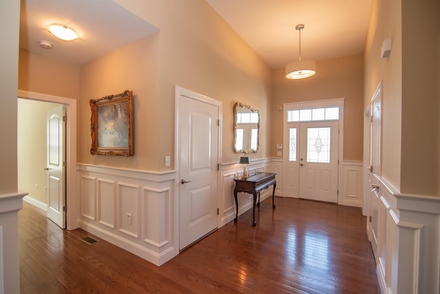 foyer entrance featuring a wainscoted wall, a decorative wall, dark wood-style flooring, and visible vents