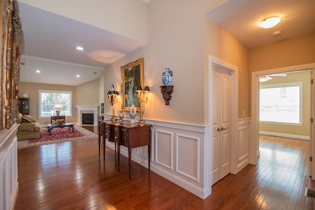 hallway with wainscoting, a decorative wall, and dark wood-style floors