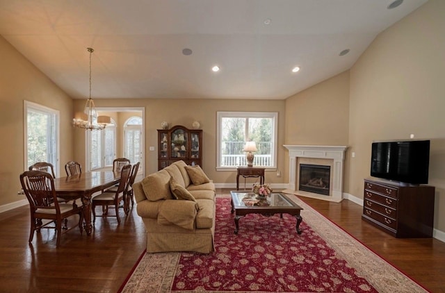 living area featuring an inviting chandelier, baseboards, a fireplace with flush hearth, dark wood-type flooring, and vaulted ceiling
