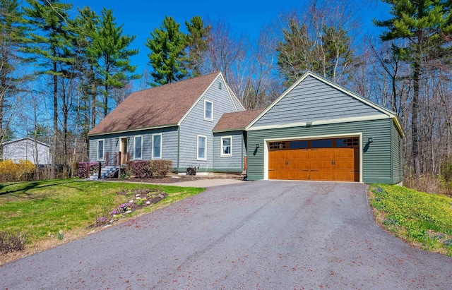 new england style home with a garage, a shingled roof, a front yard, and aphalt driveway
