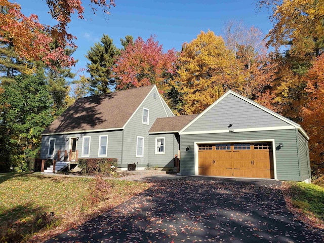 new england style home featuring a garage, roof with shingles, and driveway