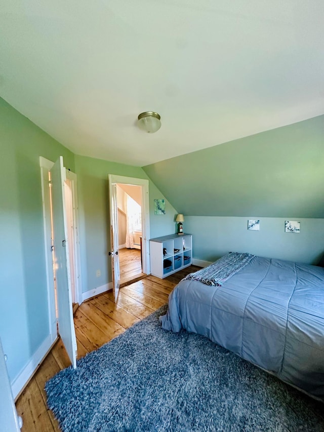 bedroom featuring baseboards, hardwood / wood-style floors, and lofted ceiling