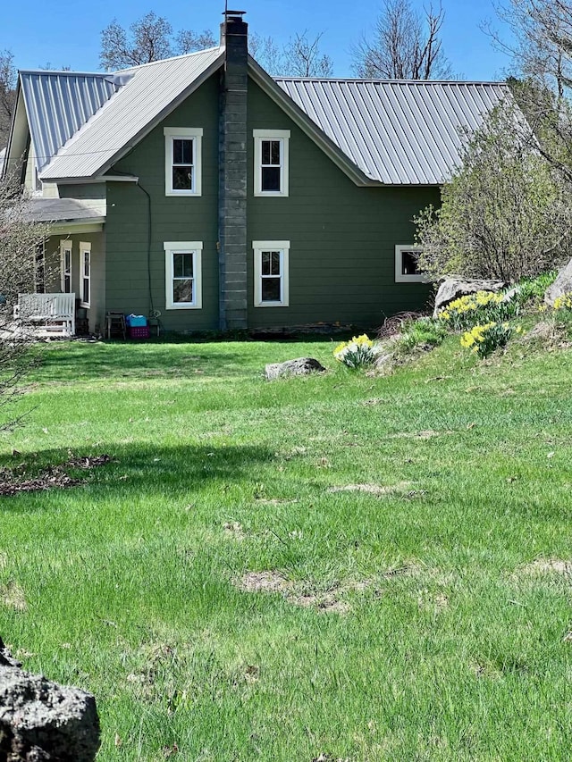 view of property exterior with a yard, a chimney, and metal roof