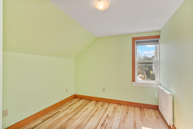 additional living space featuring baseboards, vaulted ceiling, wood finished floors, and radiator