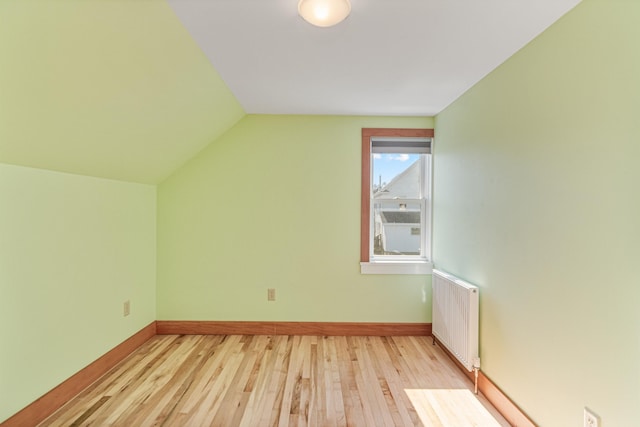 additional living space featuring radiator, baseboards, wood finished floors, and lofted ceiling