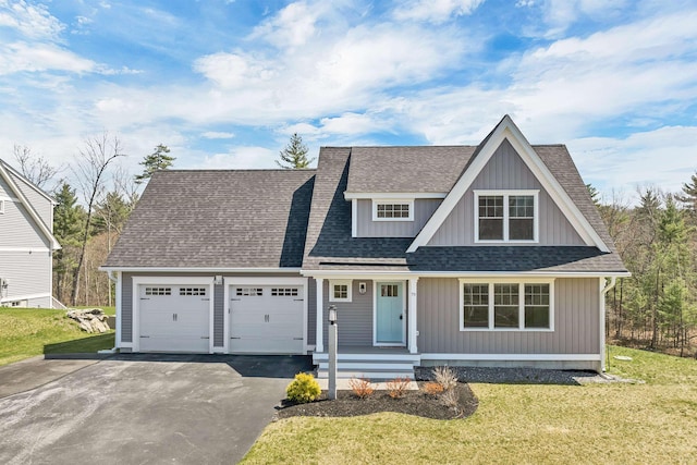 shingle-style home featuring a garage, covered porch, a front yard, a shingled roof, and driveway