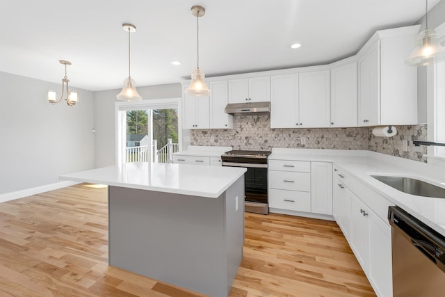 kitchen with a sink, light wood finished floors, stainless steel appliances, backsplash, and under cabinet range hood