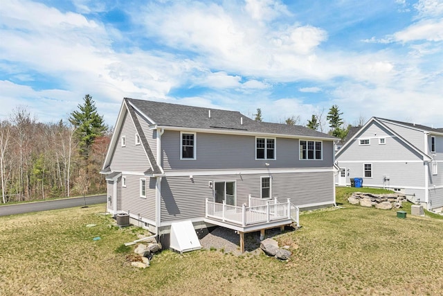 rear view of property featuring a lawn, a deck, central AC unit, and roof with shingles
