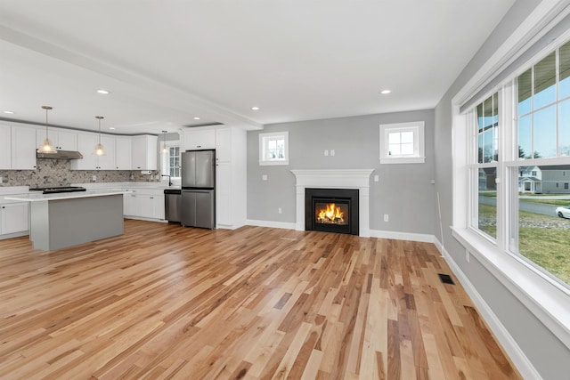 unfurnished living room with a glass covered fireplace, baseboards, light wood-style flooring, and visible vents