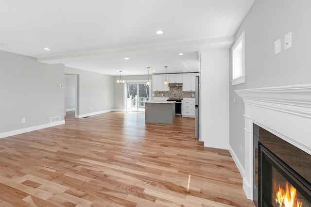 unfurnished living room featuring recessed lighting, a lit fireplace, light wood-style flooring, and visible vents