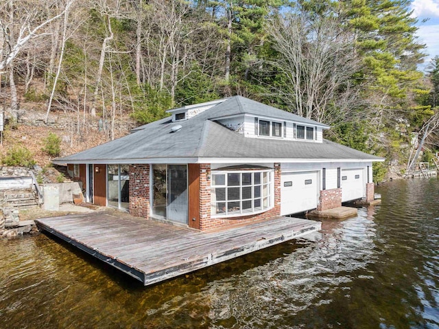 exterior space with brick siding, a water view, a shingled roof, and a garage