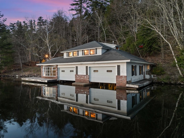 back of house at dusk with a water view, a wooded view, and a garage