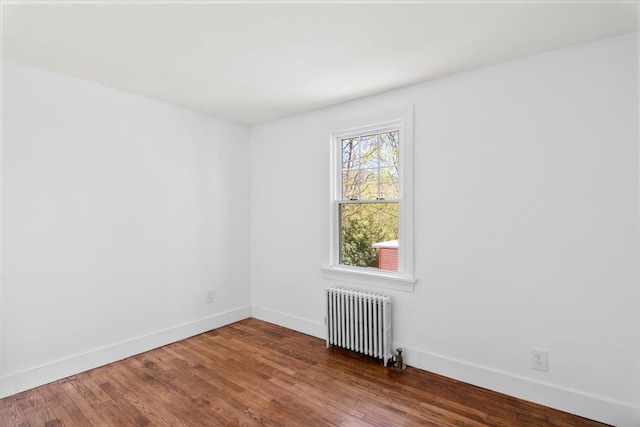 spare room with radiator, baseboards, and wood finished floors
