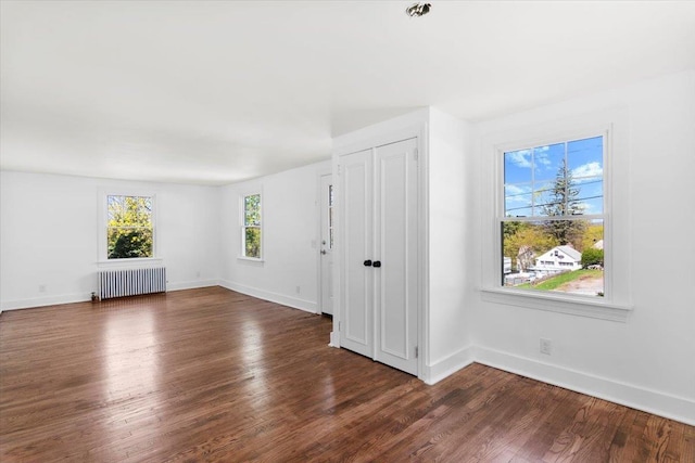 spare room featuring radiator heating unit, baseboards, and dark wood-style flooring