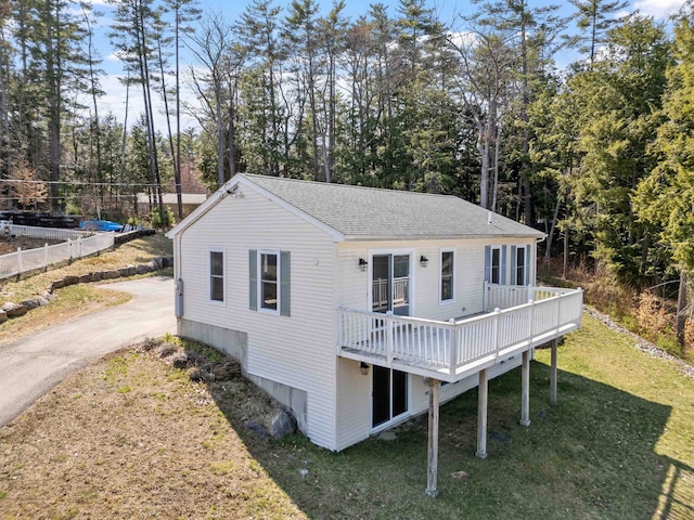 back of property with a lawn, a wooden deck, and a shingled roof