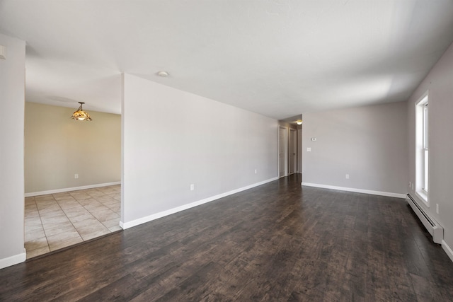 spare room featuring baseboards, a baseboard heating unit, and dark wood finished floors