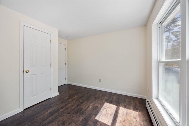 empty room with dark wood-type flooring, a baseboard radiator, baseboards, and plenty of natural light