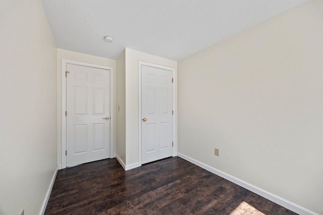 unfurnished bedroom with baseboards and dark wood-type flooring
