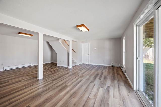 basement featuring plenty of natural light, baseboard heating, stairway, and wood finished floors