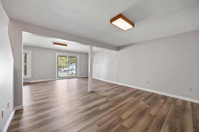 unfurnished room with baseboards, a baseboard heating unit, and wood finished floors