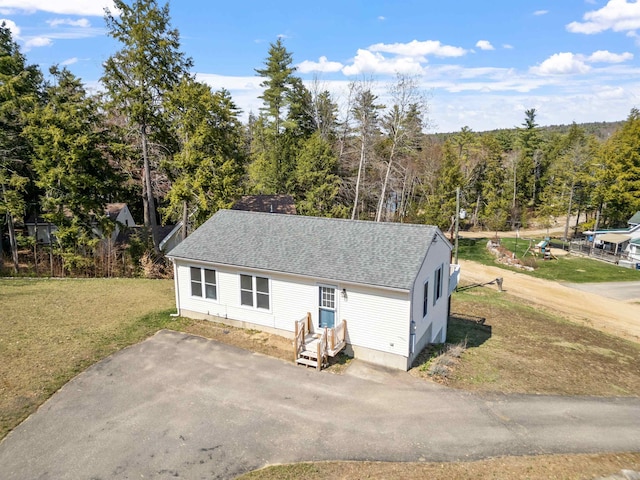 view of front of house featuring roof with shingles, entry steps, and a front lawn