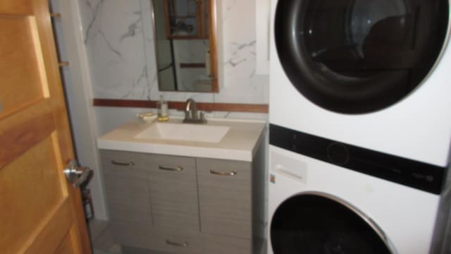 washroom featuring laundry area, stacked washer and dryer, and a sink