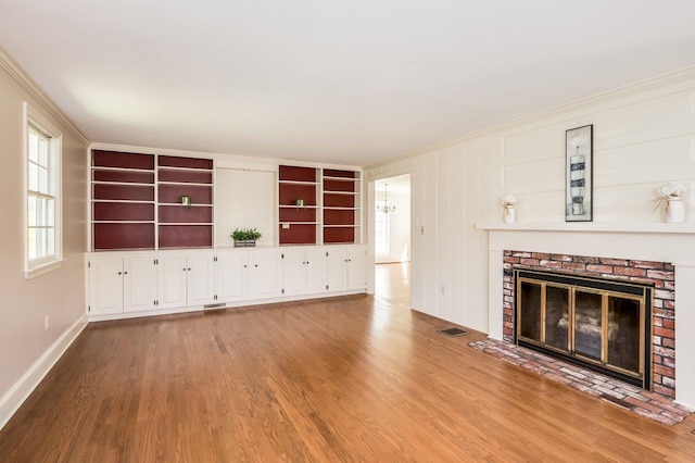 unfurnished living room featuring visible vents, crown molding, a brick fireplace, wood finished floors, and baseboards