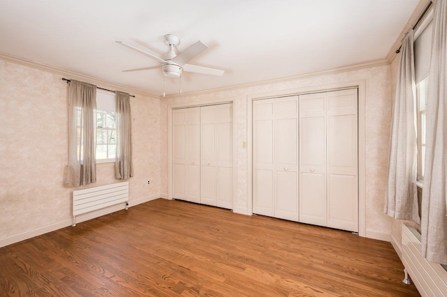 unfurnished bedroom with radiator, ornamental molding, multiple closets, and wood finished floors