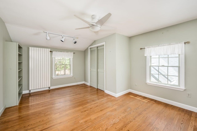 unfurnished bedroom with rail lighting, baseboards, lofted ceiling, light wood-type flooring, and a closet