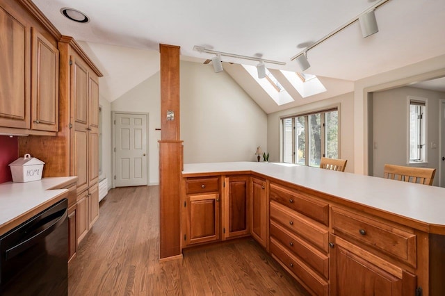 kitchen featuring light countertops, track lighting, lofted ceiling with skylight, and dishwasher