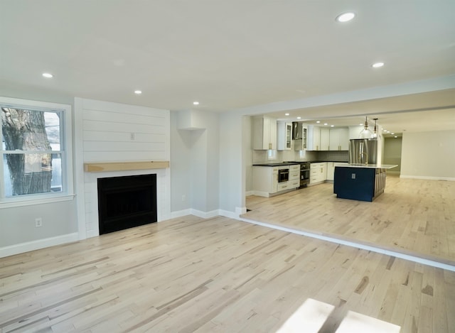 unfurnished living room featuring recessed lighting, baseboards, light wood-style flooring, and a fireplace