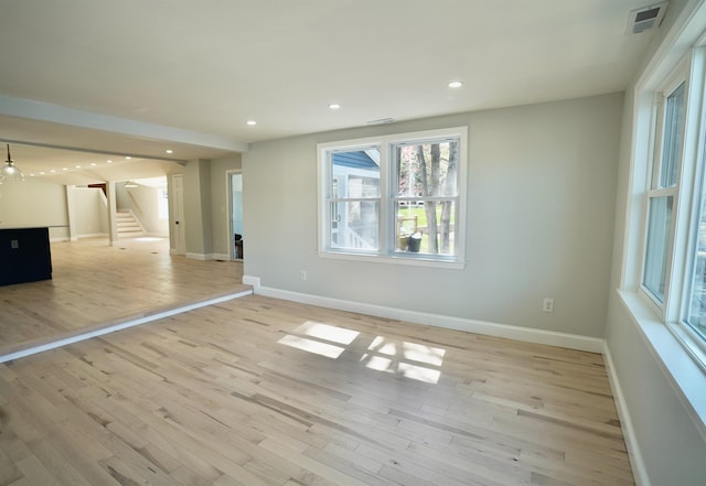 unfurnished living room featuring visible vents, stairs, baseboards, and a wealth of natural light